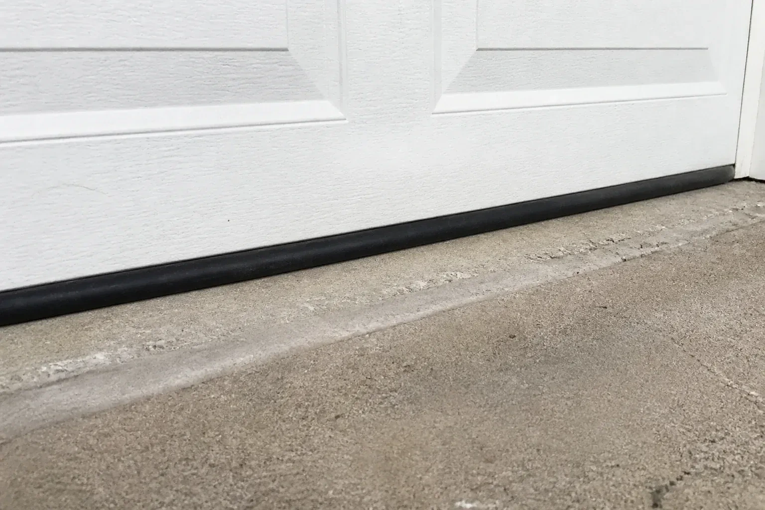 Black bottom seal along a closed white garage door at a concrete threshold. — Garage Door Bottom Seal Replacement, Mississauga